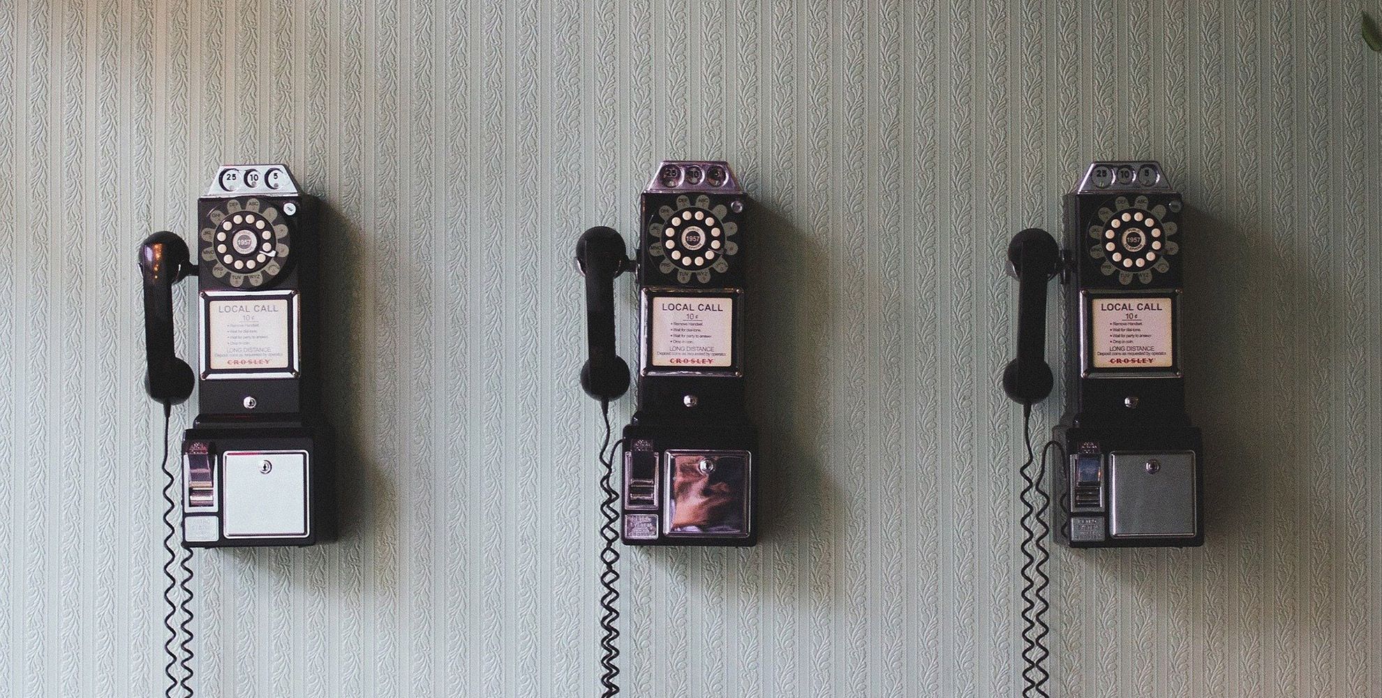 Drei historische Wandtelefone vor einer gemusterten Tapete