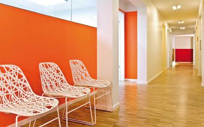 Wartebereich mit orangefarbener Akzentwand und weißen Stühlen