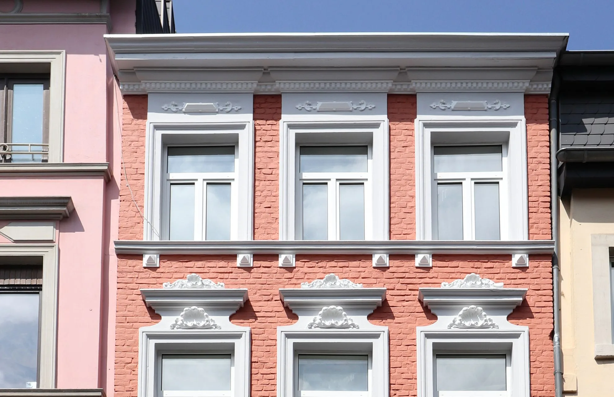 Rote Fassade mit weißen Fensterrahmen und profilierten Gesimsen